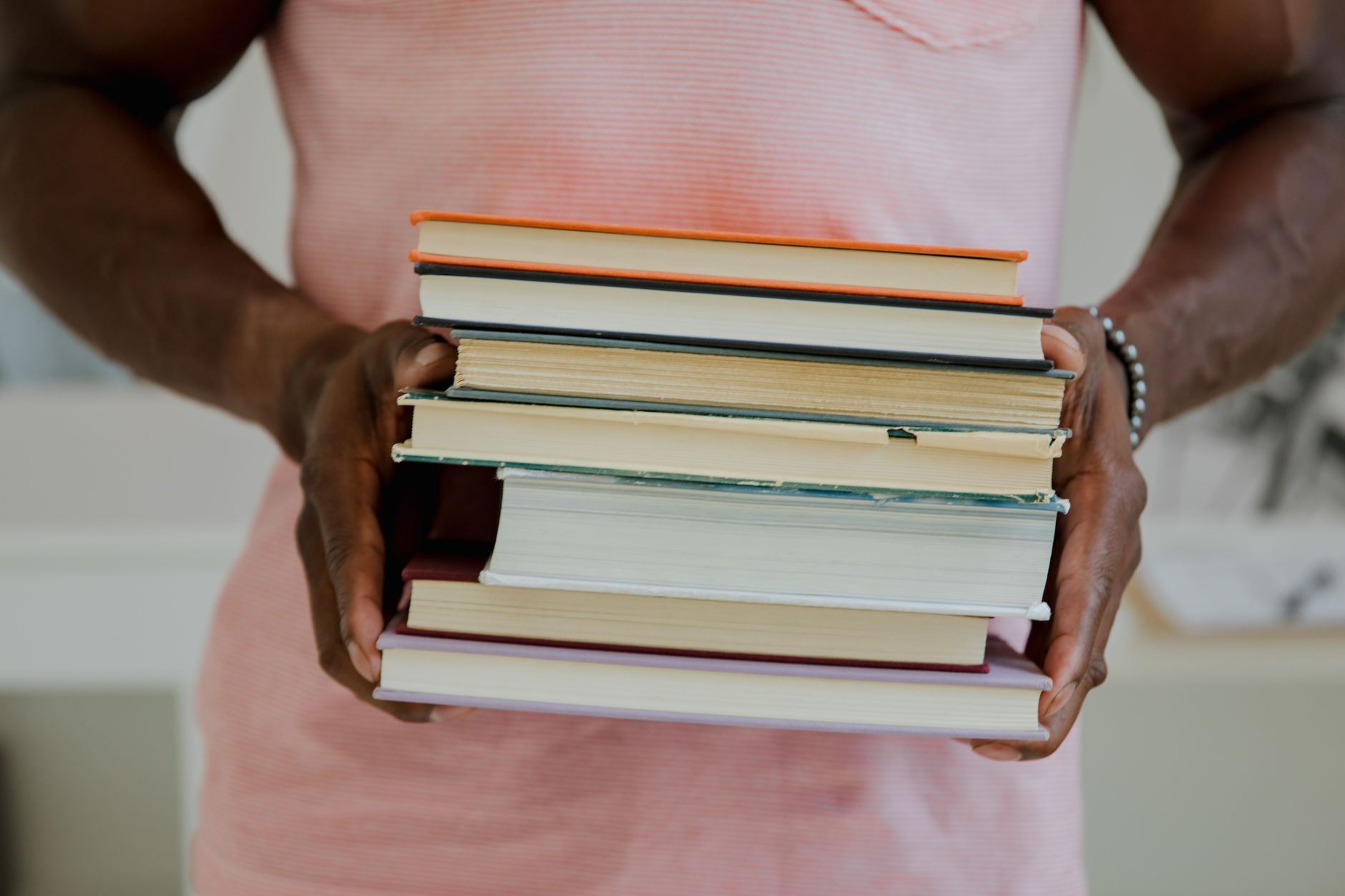 A person holding a stack of seven books indoors. Perfect for educational themes.