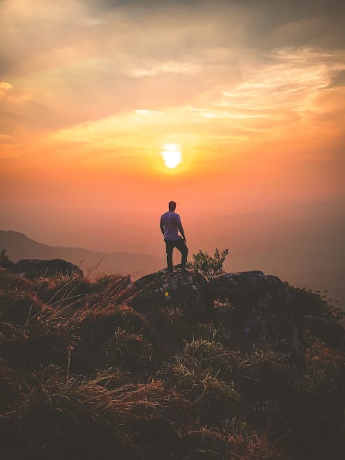 бесплатная Человек, стоящий на скале во время заката Стоковое фото