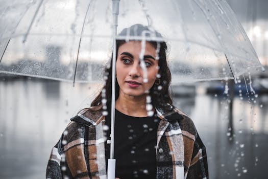 A fashionable woman holds a clear umbrella during a rainy day, showcasing modern style.