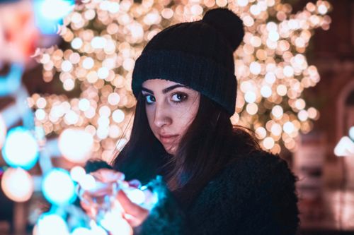 Free A woman in a beanie poses with glowing lights at night, creating a magical ambiance. Stock Photo