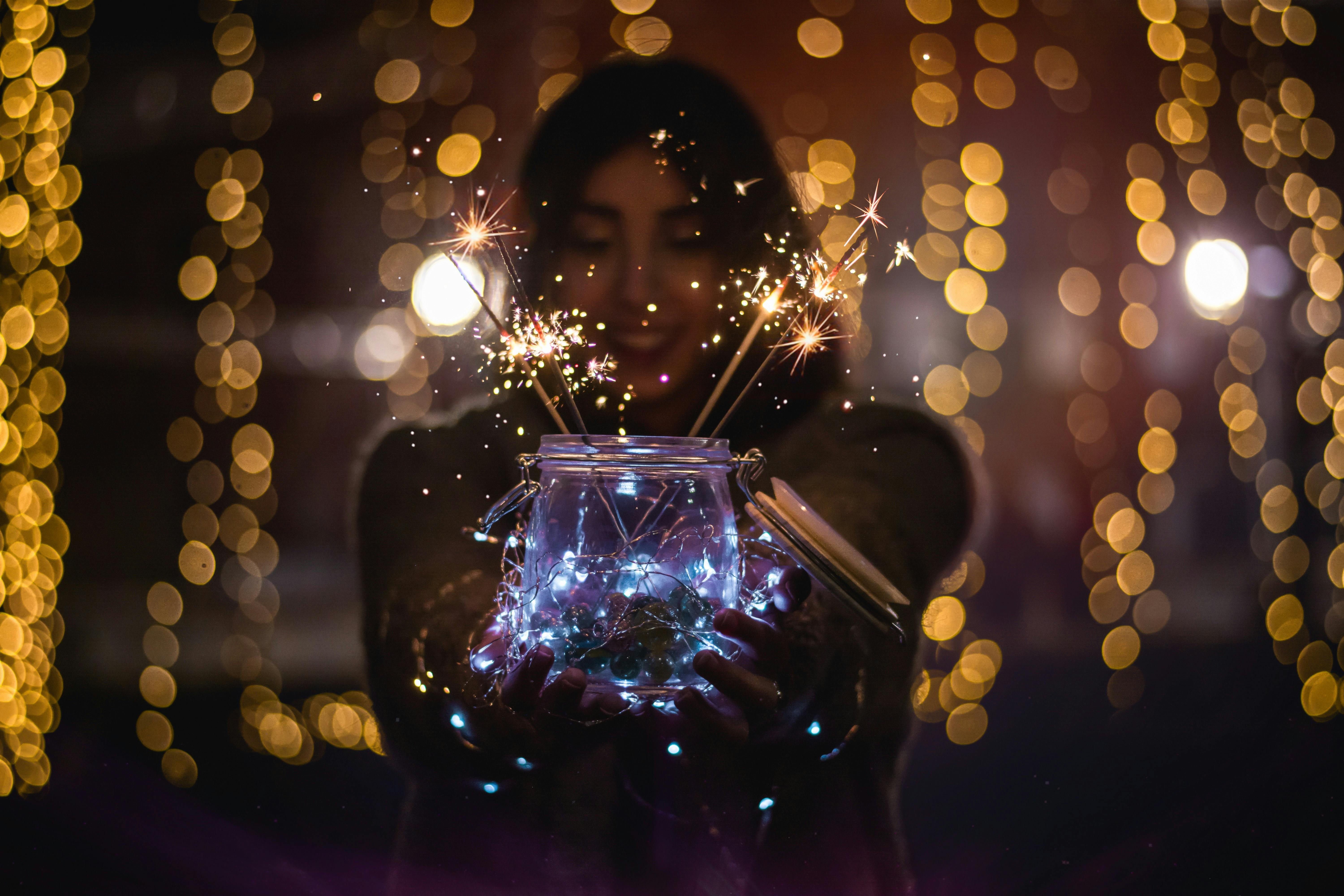 woman holding clear glass jar with sparklers in the dark 