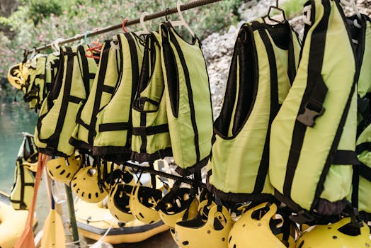 A selection of green life vests and yellow helmets hanging outdoors, ideal for water sports.
