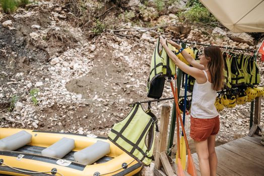 A woman arranges life jackets by a kayak, preparing for a summer adventure outdoors.