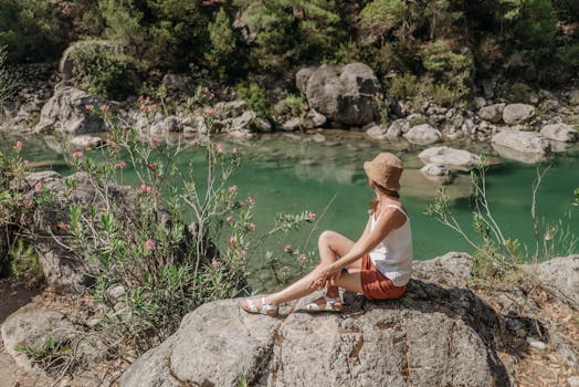 A woman enjoys a peaceful moment by a serene river surrounded by rocks and greenery.