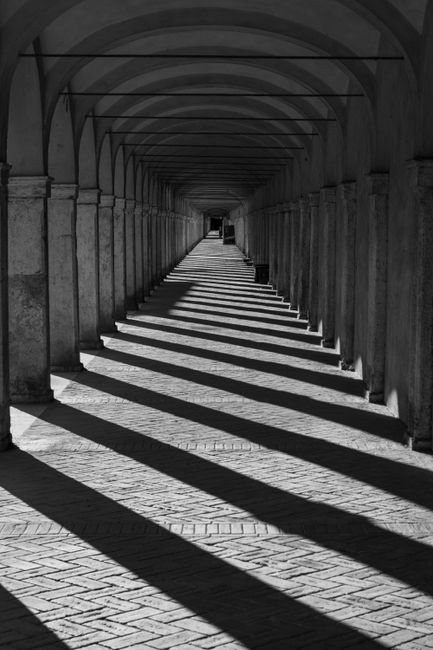 Black and white photo of a historic arched corridor with dramatic shadows.