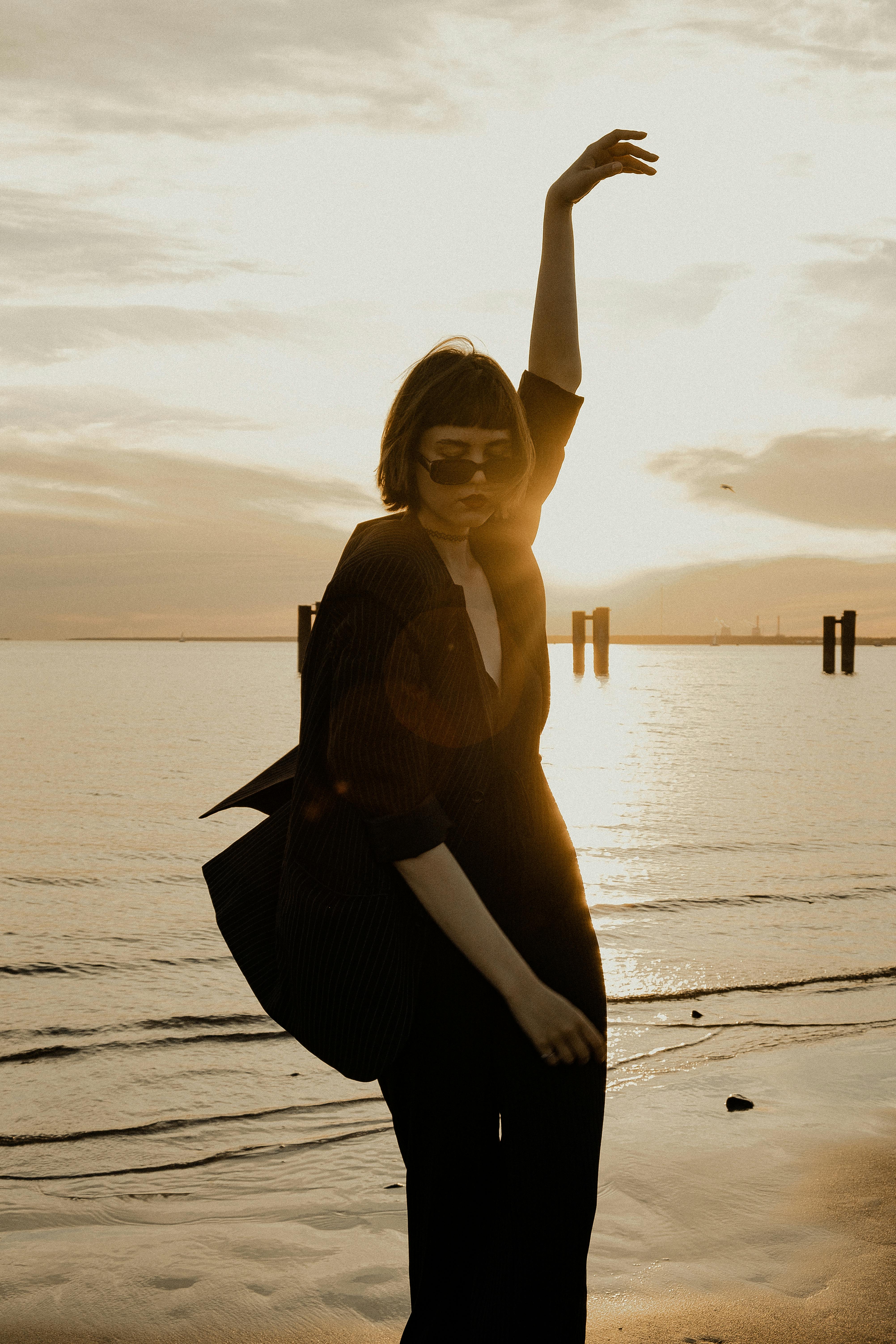 A stylish woman in sunglasses poses on the shore at sunset in Saint Petersburg, Russia.