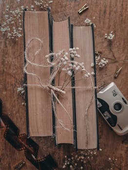 Rustic flat lay of vintage books, film camera, flowers, and film strips on wooden table.