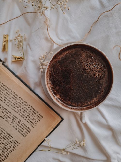 Free A warm coffee cup and open book in a serene flat lay setting with delicate flowers. Stock Photo