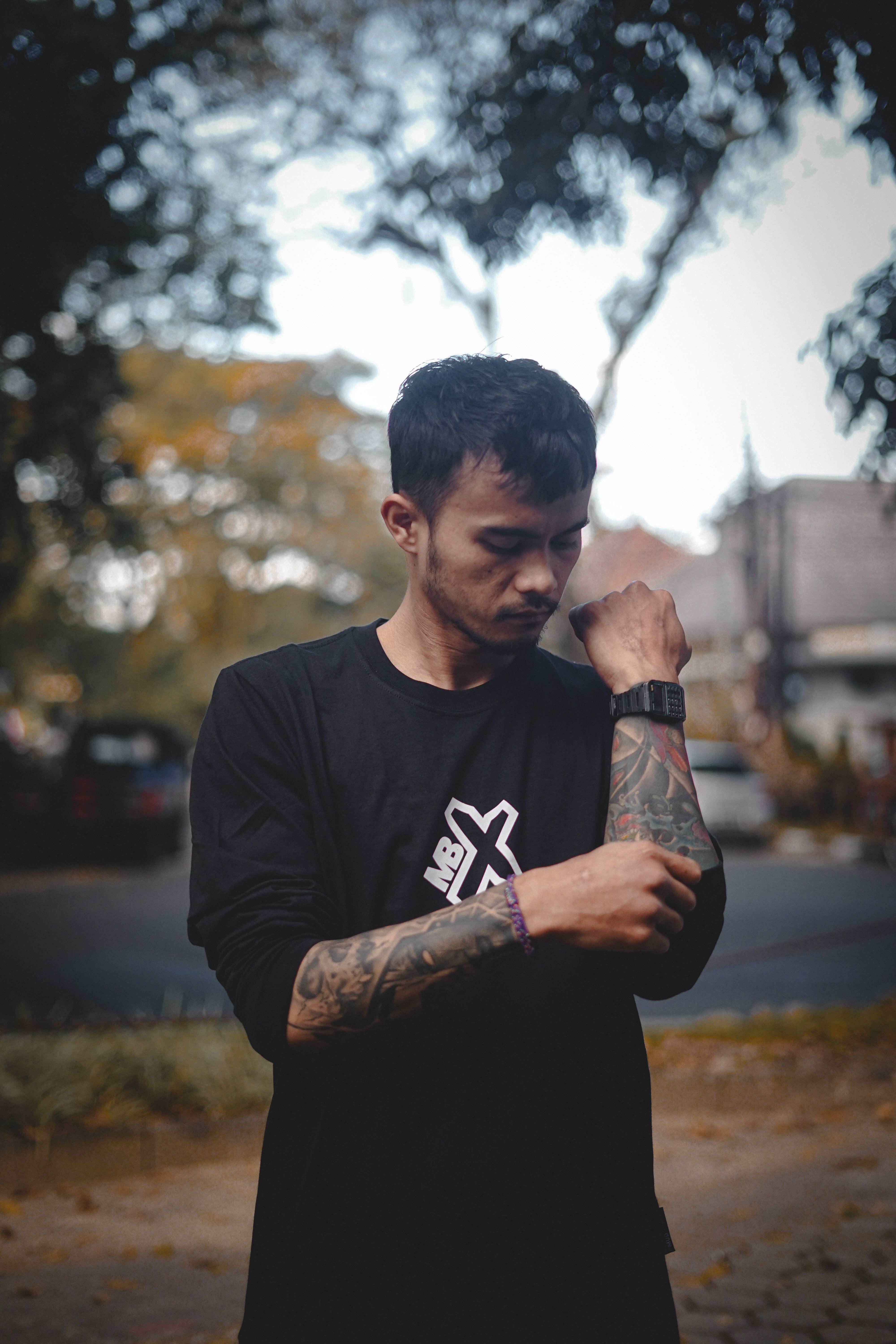 Close-up portrait of a tattooed man adjusting his black shirt during the day.