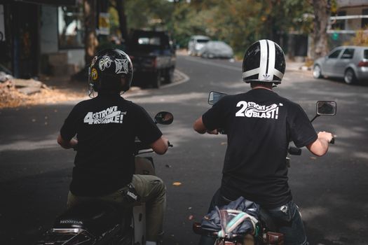 Two motorcyclists in black shirts and helmets riding down an urban street.