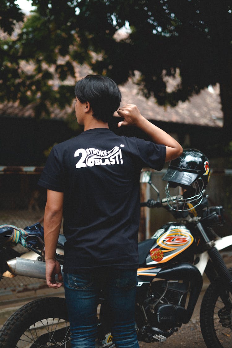 Man Standing Near His Motorcycle Pointing On Back Of His Shirt