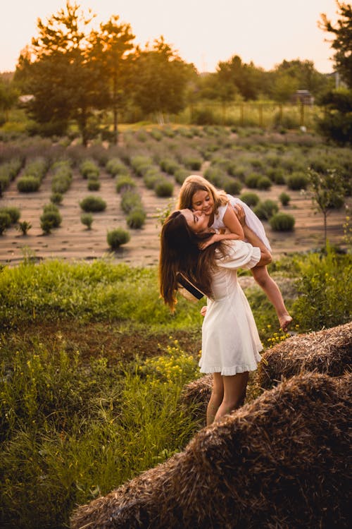 Free A Woman in White Dress Carrying Her Daughter while Standing on the Field Stock Photo