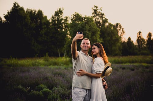 Romantic Couple Taking Photo of Themselves using a Cellphone while Standing on Flower Field