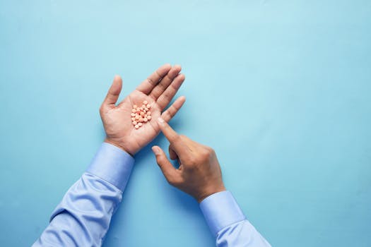 Close-up of hands holding pills on blue surface, illustrating medication and healthcare concept.