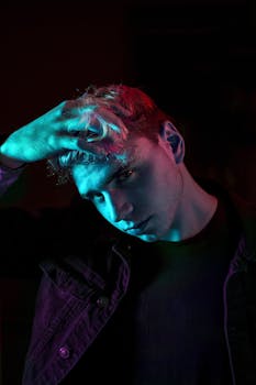 Stylish portrait of a young man with dramatic colorful lighting in a dark setting.