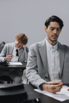 Business professionals in gray suits attending an office meeting, taking notes.