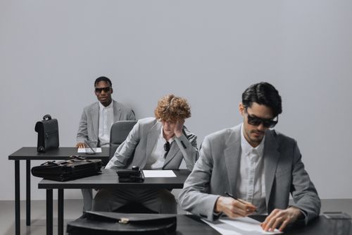 Free Three men in gray suits writing an exam indoors. Focus on business attire and concentration. Stock Photo
