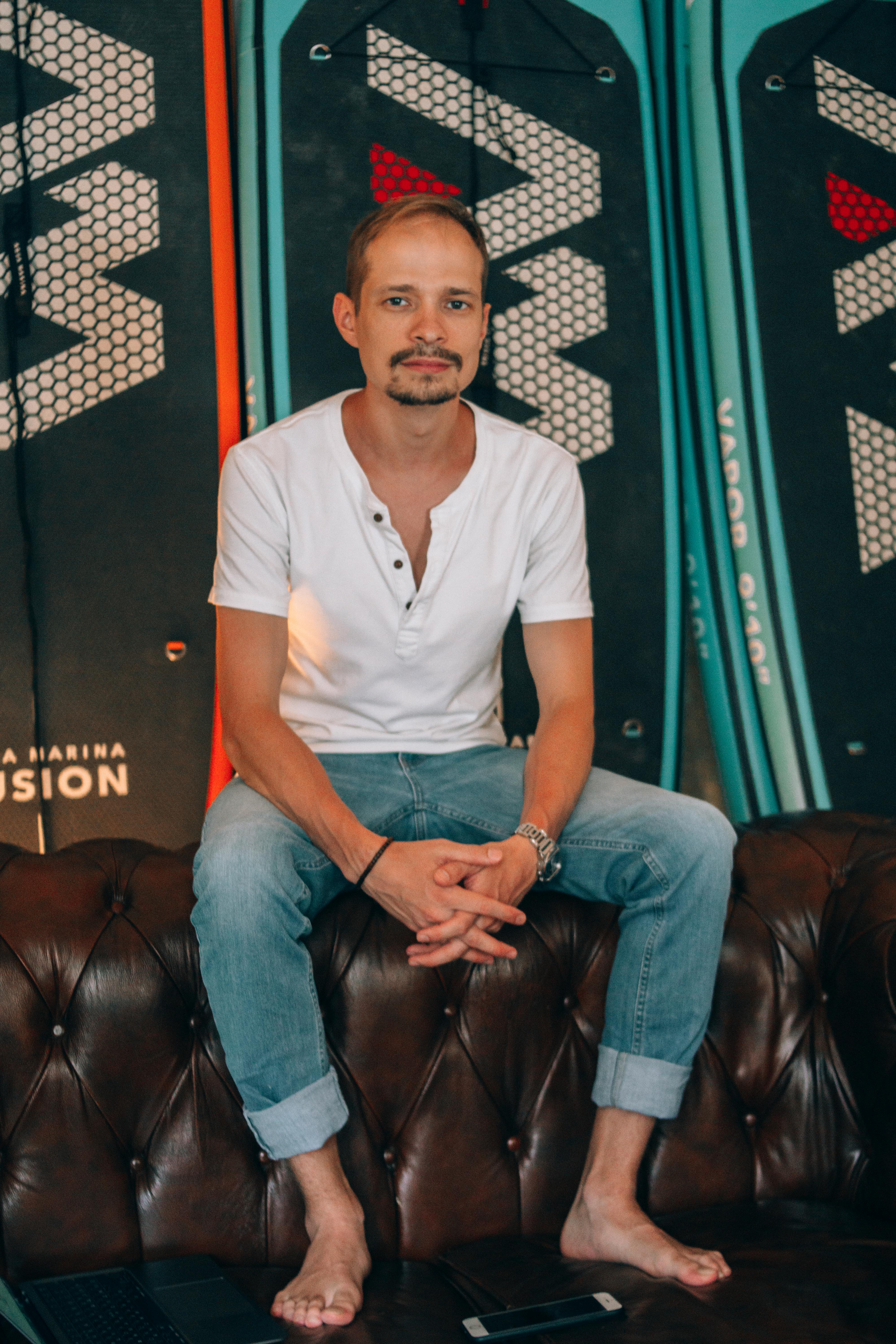 Man sitting barefoot on couch with surfboards in background.