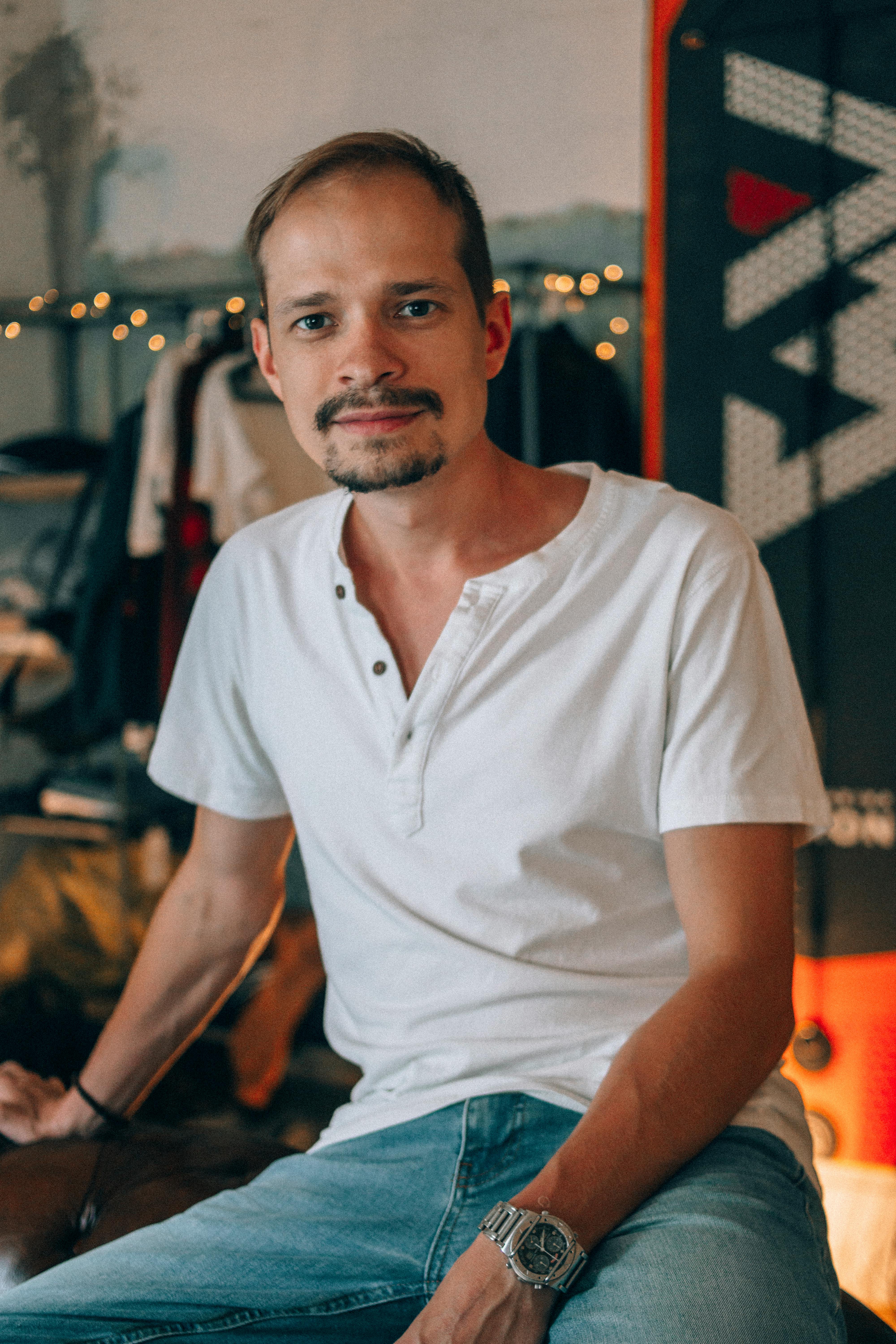 Close-up portrait of a man in a relaxed setting, wearing a white shirt and jeans.