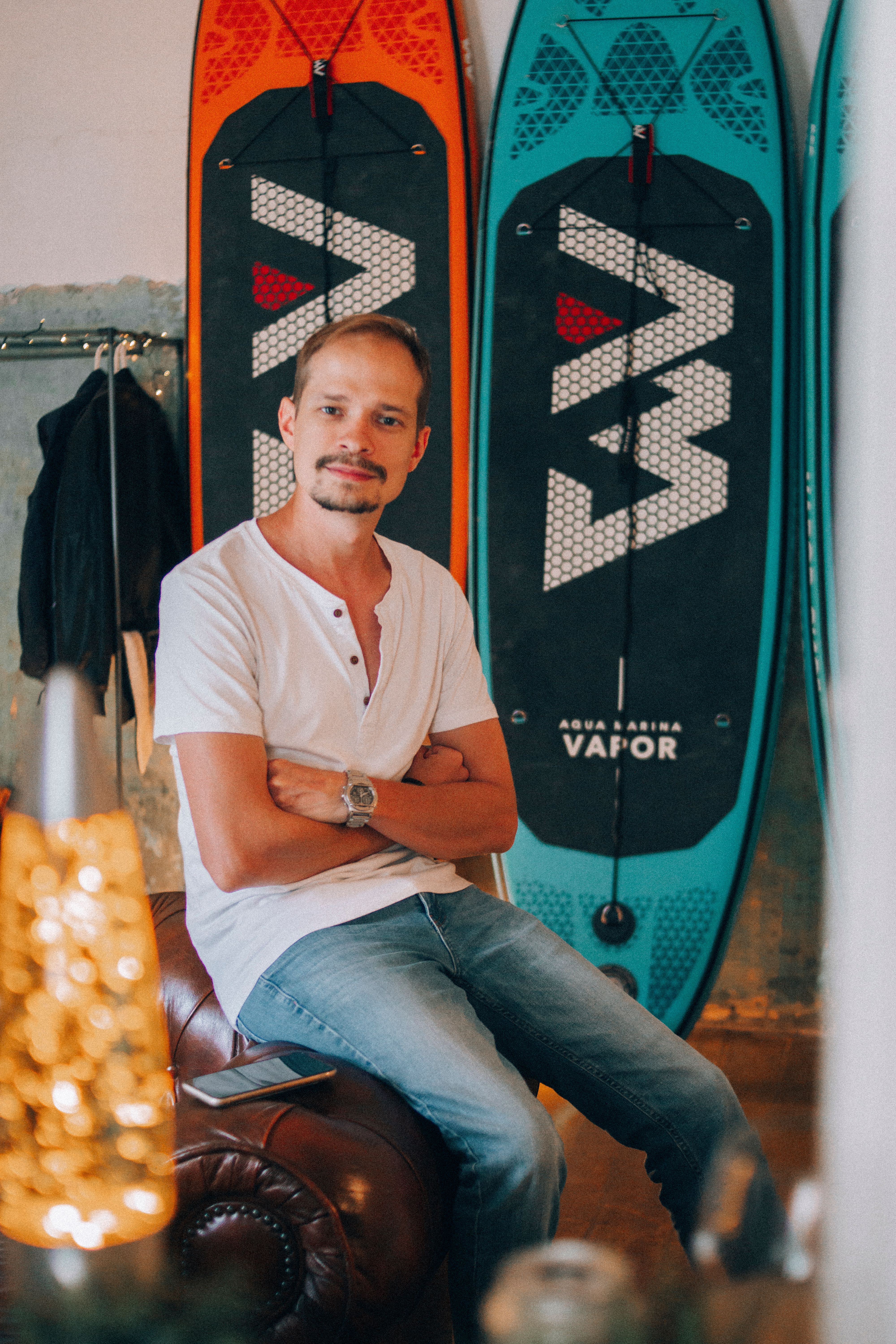 Casual man sitting on a leather couch indoors with colorful surfboards in the background.