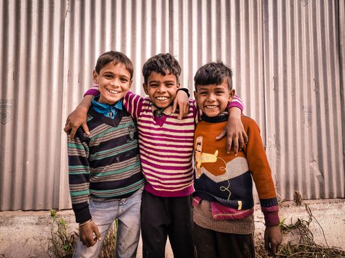 Free Three cheerful boys with arms around each other, smiling brightly against a corrugated background. Stock Photo
