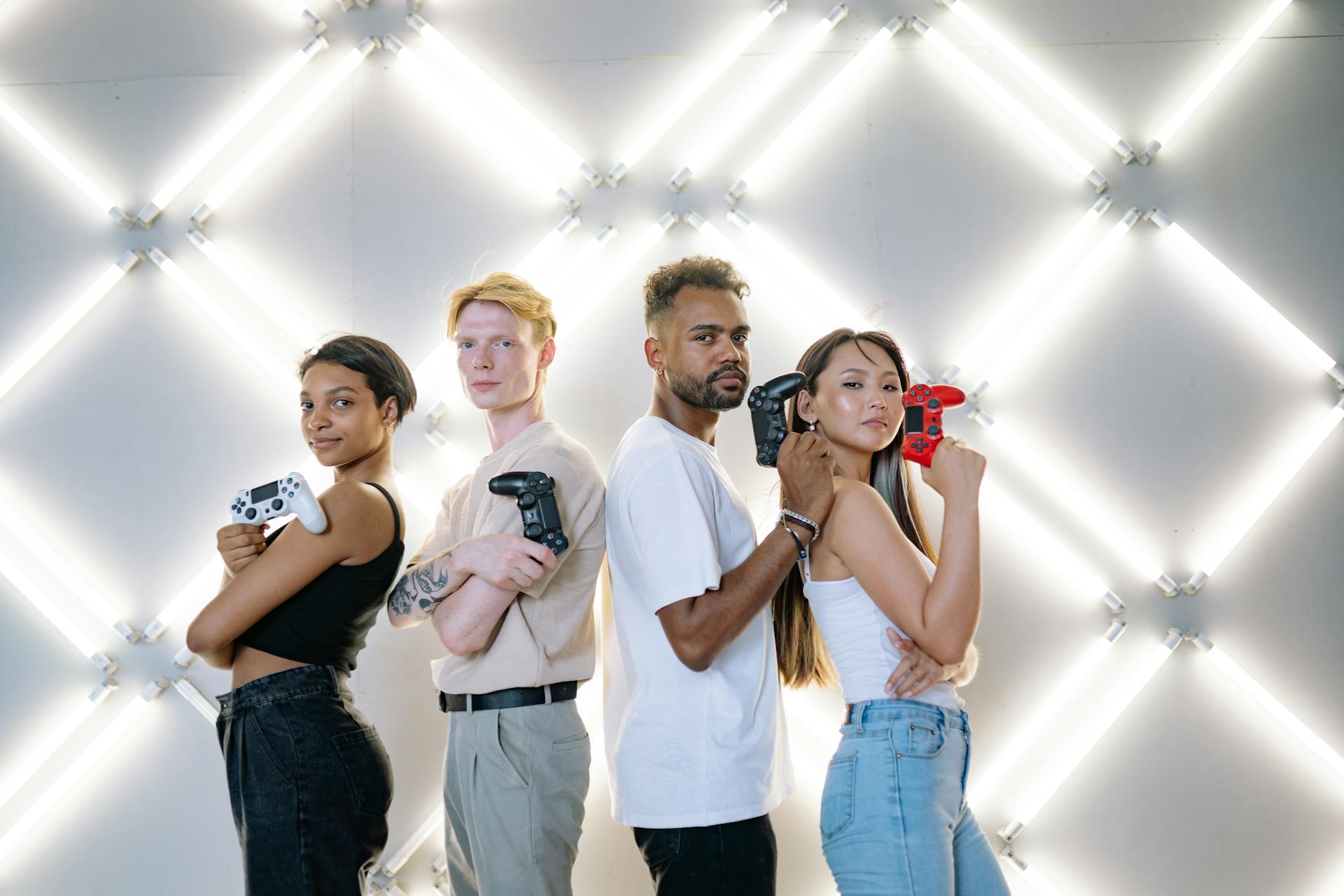 Four diverse friends posing confidently with game controllers against a modern LED backdrop.