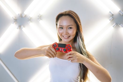 Smiling woman posing with a red game controller against modern abstract lights.