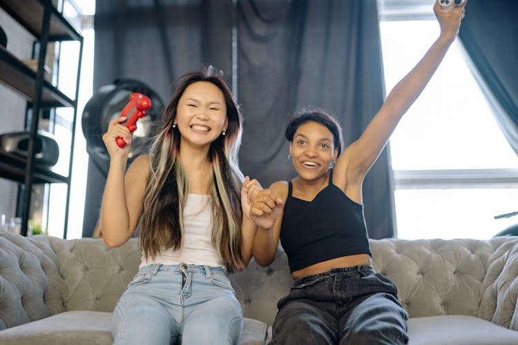 Women Sitting On Sofa Holding Game Controllers Cheering