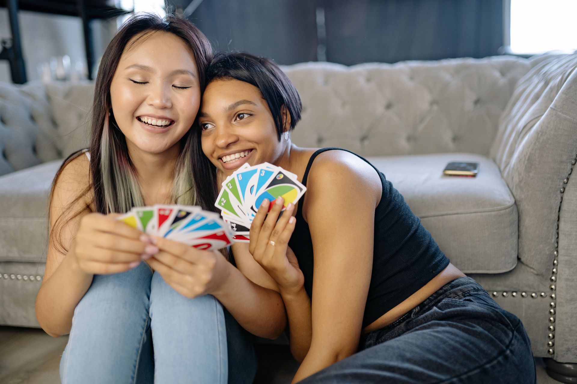 Two diverse young women enjoying a lively game of Uno at home, capturing joyful friendship and leisure time.