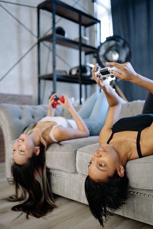 Two Women Playing Video Games while Lying on the Sofa