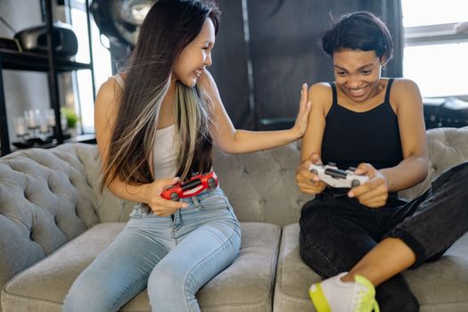 Two women having fun playing video games on a sofa indoors, showcasing friendship and leisure time.