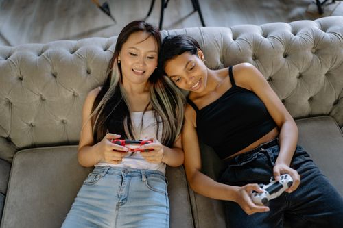 Free Two women relaxing and playing video games on a comfortable sofa together. Stock Photo