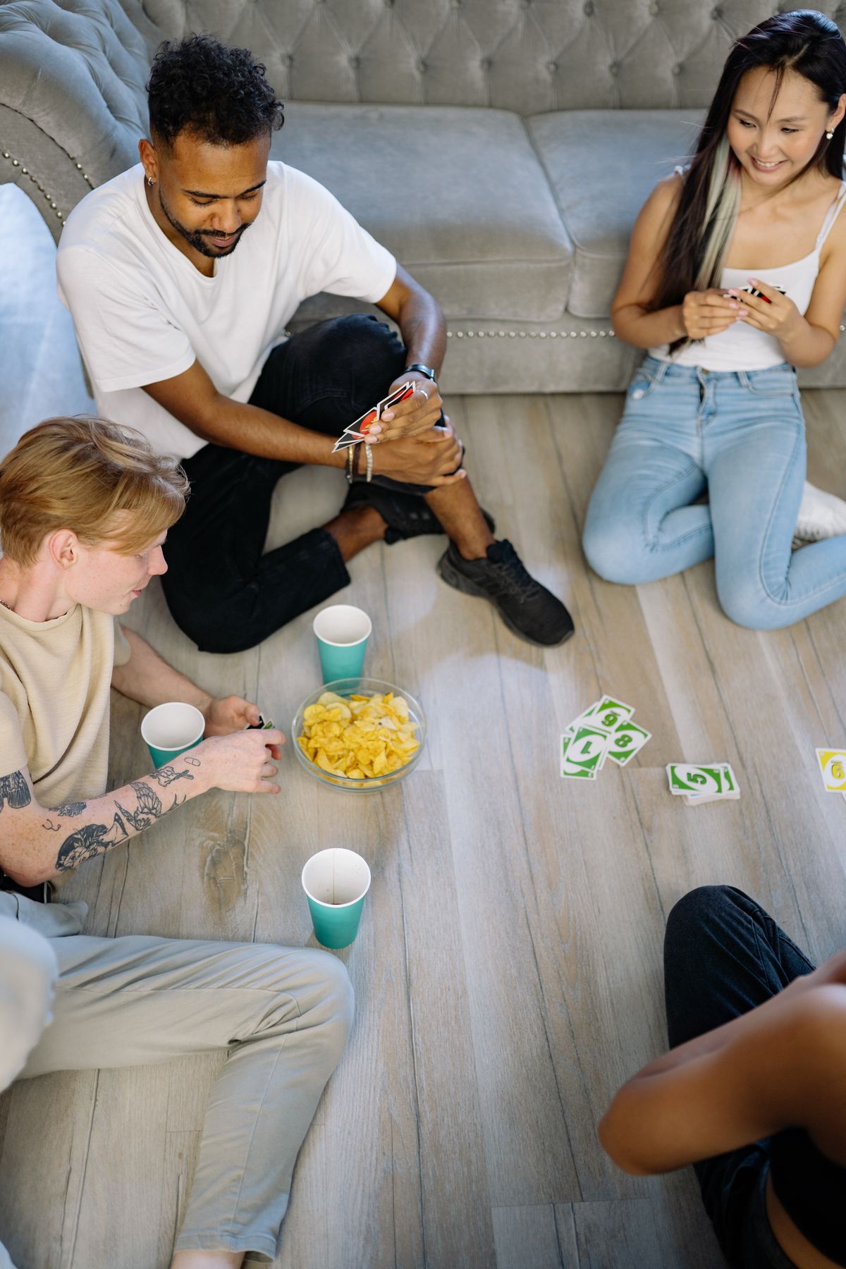 A group of friends playing Uno cards on the floor indoors