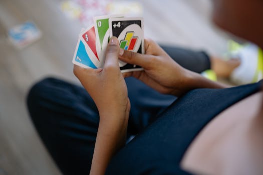 Person playing Uno cards, focusing on colorful cards and hands in a casual setting.