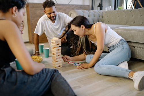 Free A group of friends playing Jenga on the living room floor, sharing a joyful moment. Stock Photo