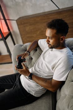 Young man sitting on sofa, focused on video gaming with a controller.