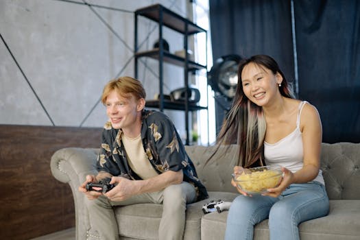 A man and woman enjoying a video game session with snacks on a sofa indoors.