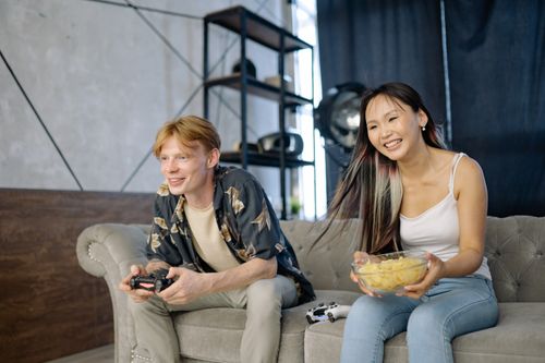 Free A man and woman enjoying a video game session with snacks on a sofa indoors. Stock Photo