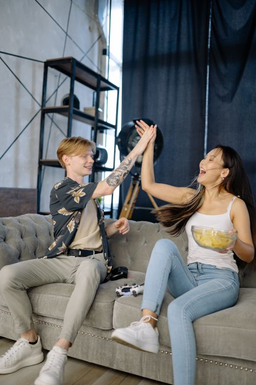 Free Two friends high-five on a sofa, celebrating with joy and laughter indoors. Stock Photo