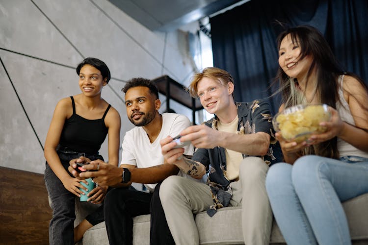 A Group Of Friends Playing Video Game While Sitting On A Sofa