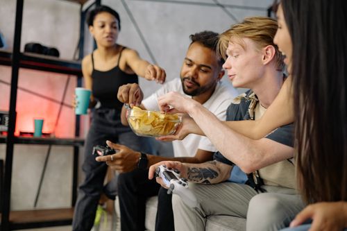 Free A group of friends enjoy snacks and gaming indoors, showcasing leisure and diversity. Stock Photo