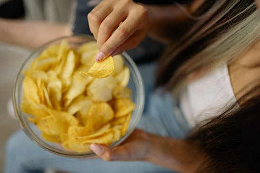 A person reaches for potato chips in a bowl, capturing the essence of snacking.