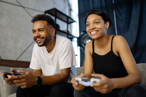 Free A couple playing video games on a sofa, engaged and smiling indoors. Stock Photo