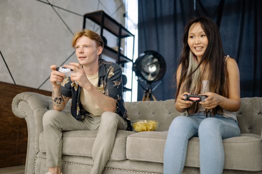 Two friends engaged in video gaming at home, enjoying leisure time on a comfortable couch.