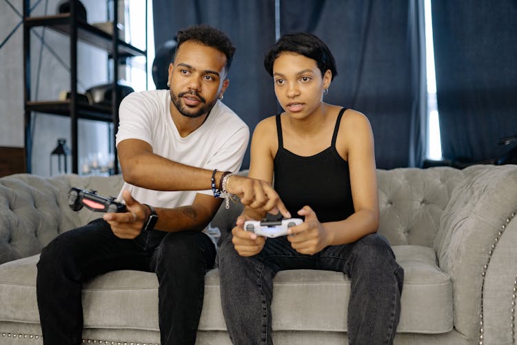 A Man And A Woman Playing Video Games While Sitting On The Sofa