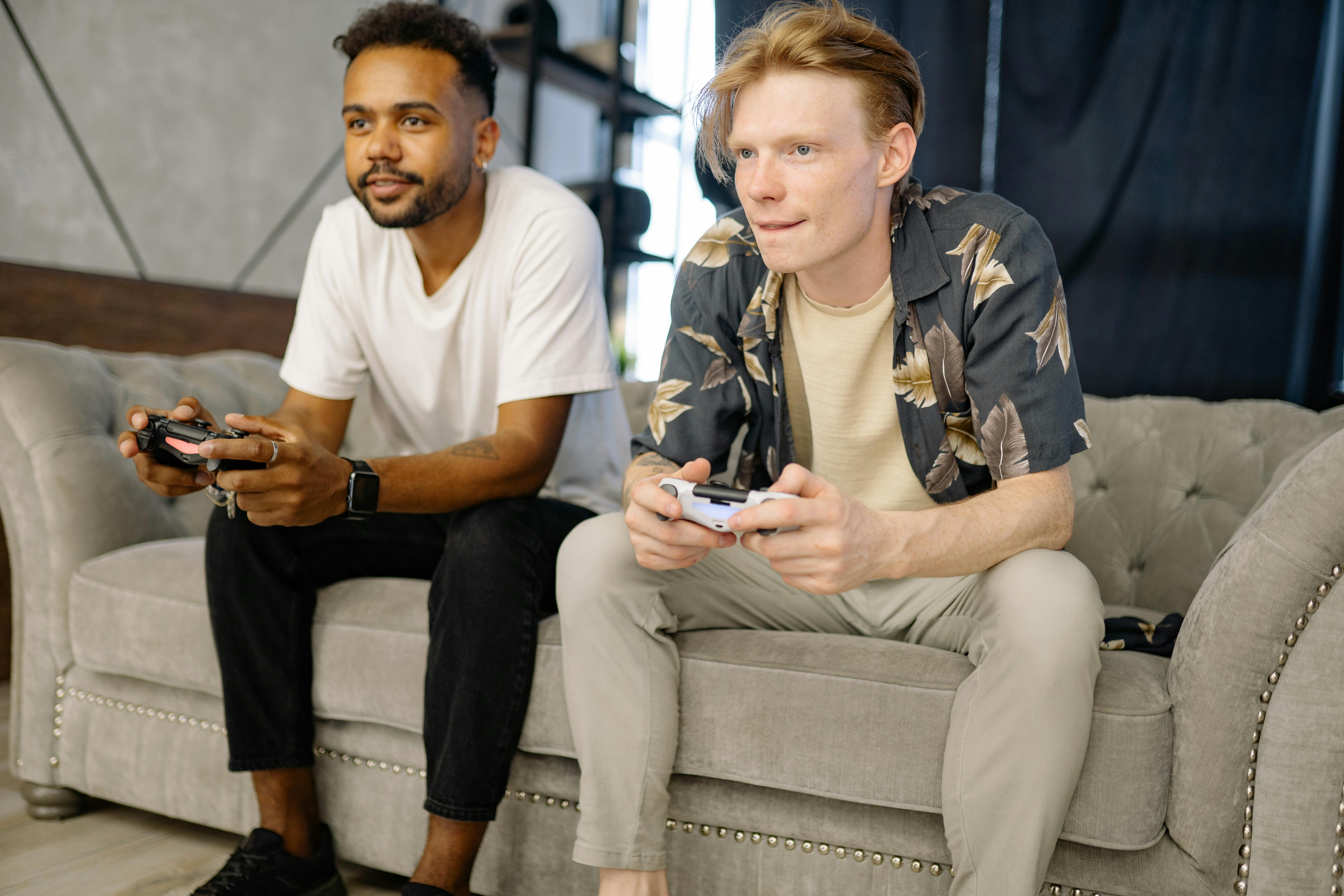 two men playing video games while sitting on the sofa