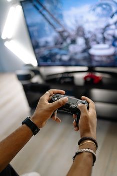 Close-up of hands holding a game controller while immersed in gaming on a large TV screen.