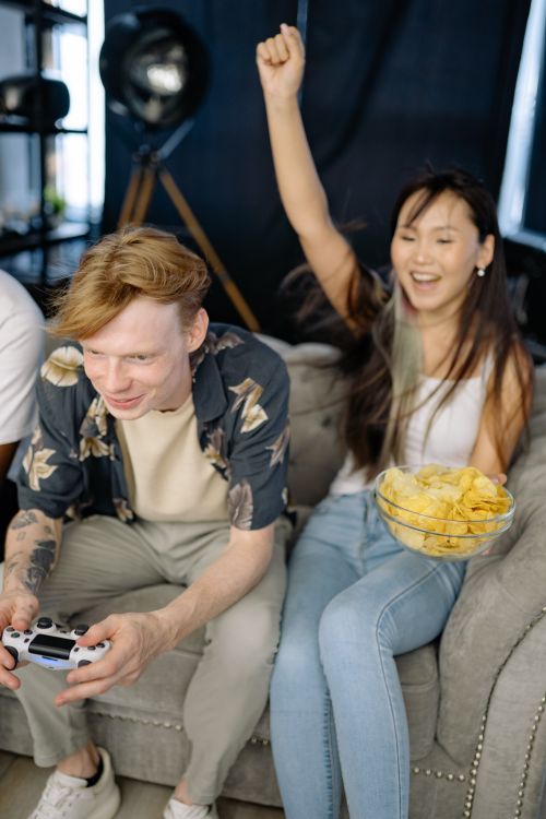 Free Two young friends gaming on a couch indoors, having fun and enjoying snacks. Stock Photo