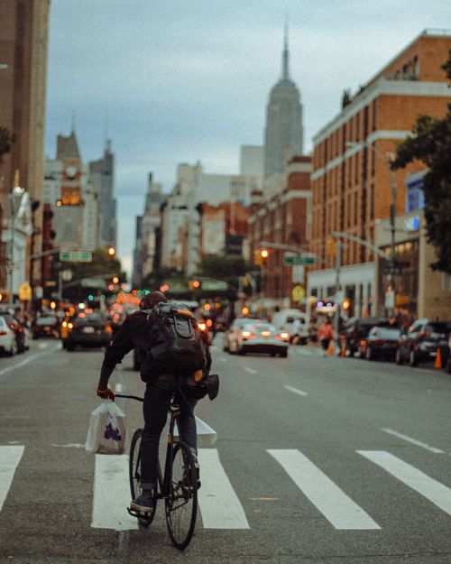 Free A cyclist rides through bustling New York City streets at dusk with the Empire State Building in view. Stock Photo