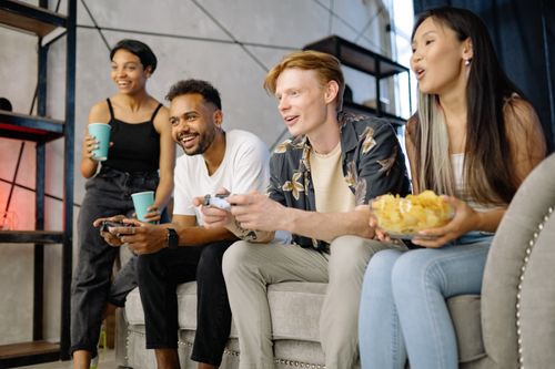 Free Group of friends playing video games, laughing and enjoying snacks indoors. Stock Photo